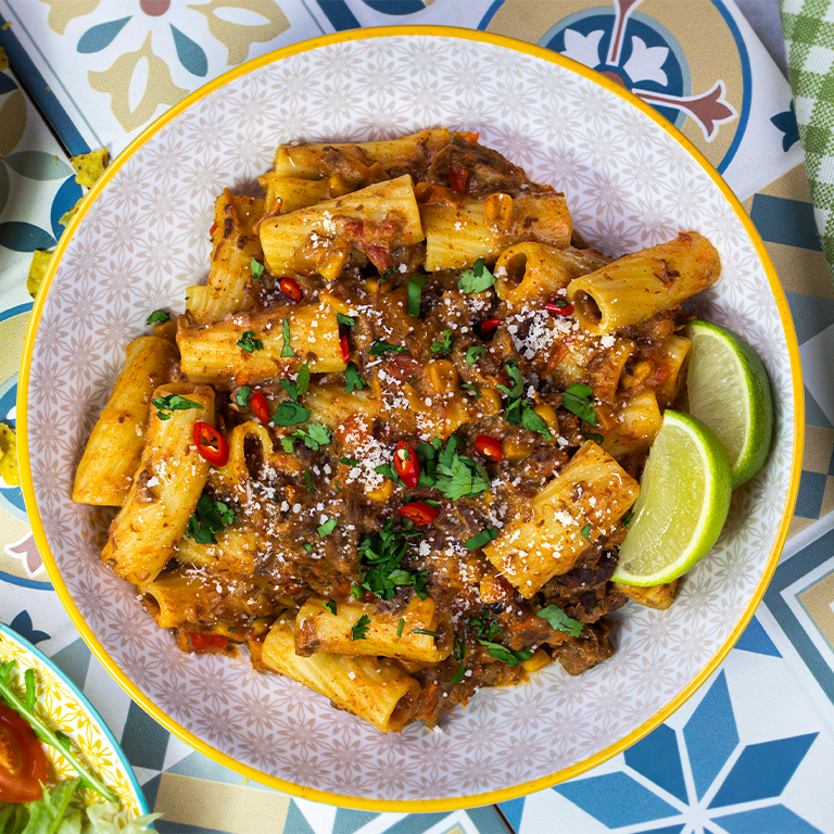 Bowl of Chipotle Beef Pasta made with Chilli Con Carne Gourmet Sause Mix on a table with colourful décor