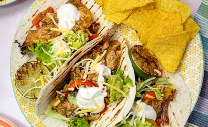 Plate of Gordon Rhodes Sticky Brisket of Beef Mexican-style tacos with guacamole, sour cream, red onion and tomato.