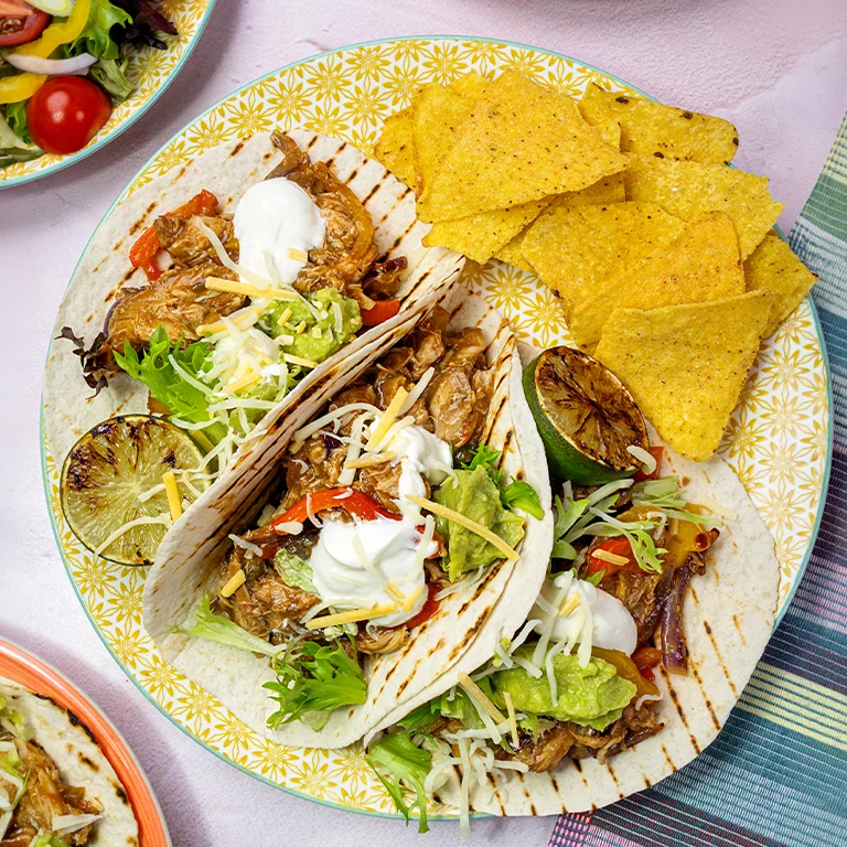 Plate of Gordon Rhodes Sticky Brisket of Beef Mexican-style tacos with guacamole, sour cream, red onion and tomato.